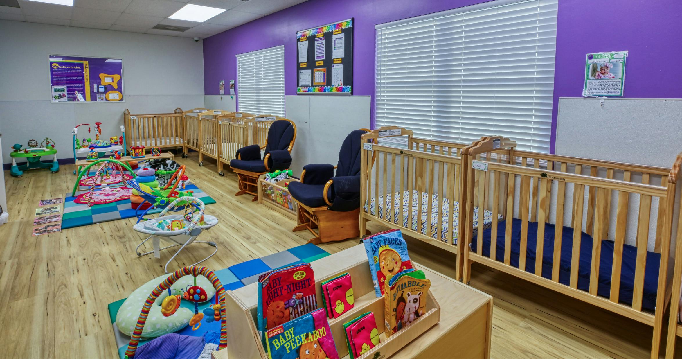 cribs in an infant classroom with playmats and books