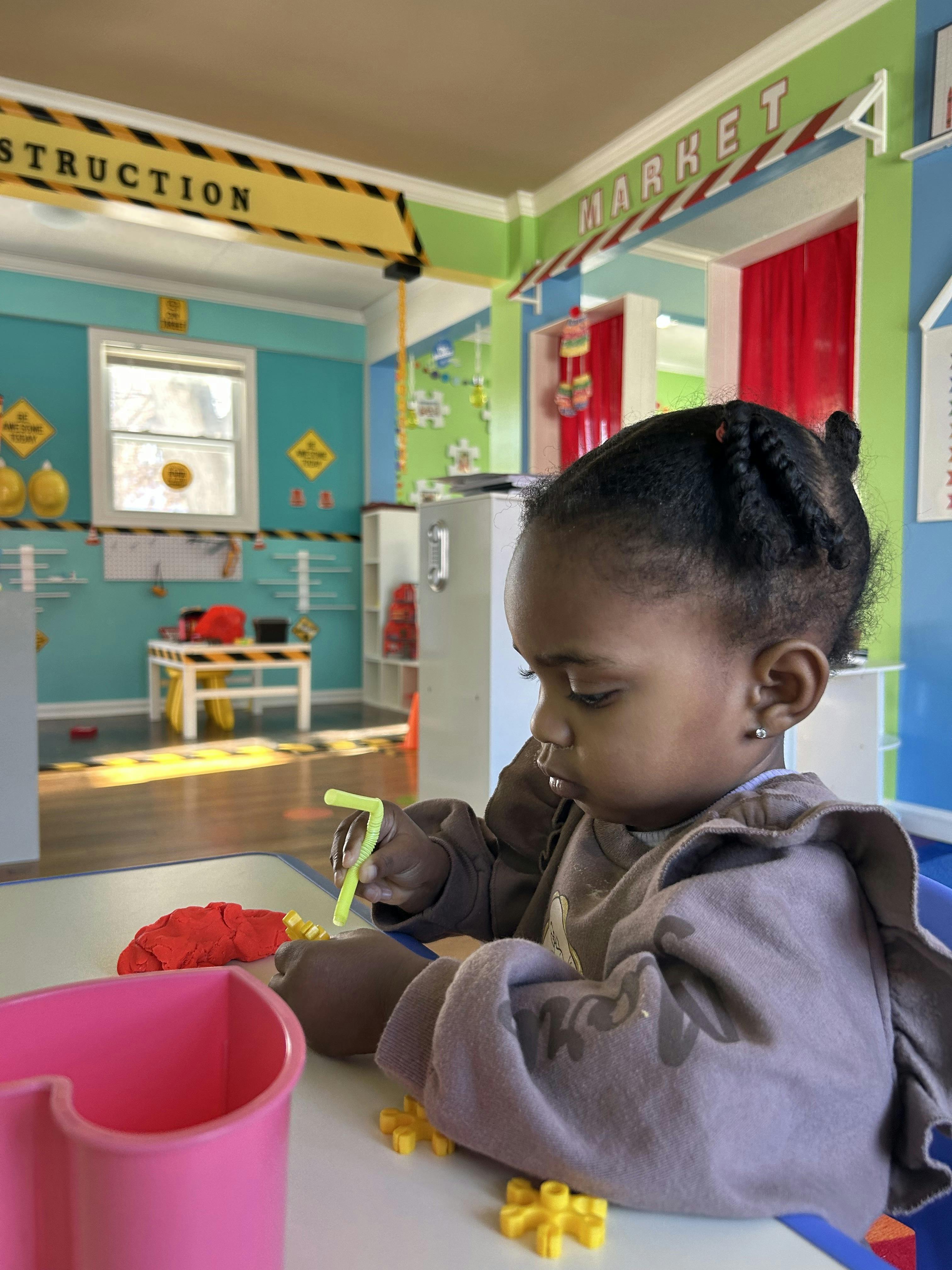 Child playing with red clay and a bent straw at a table