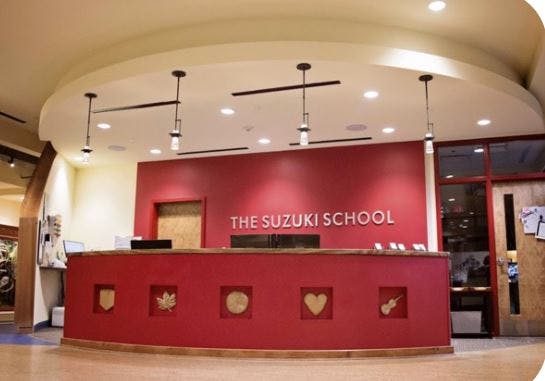 Red reception desk with "THE SUZUKI SCHOOL" on the wall behind it