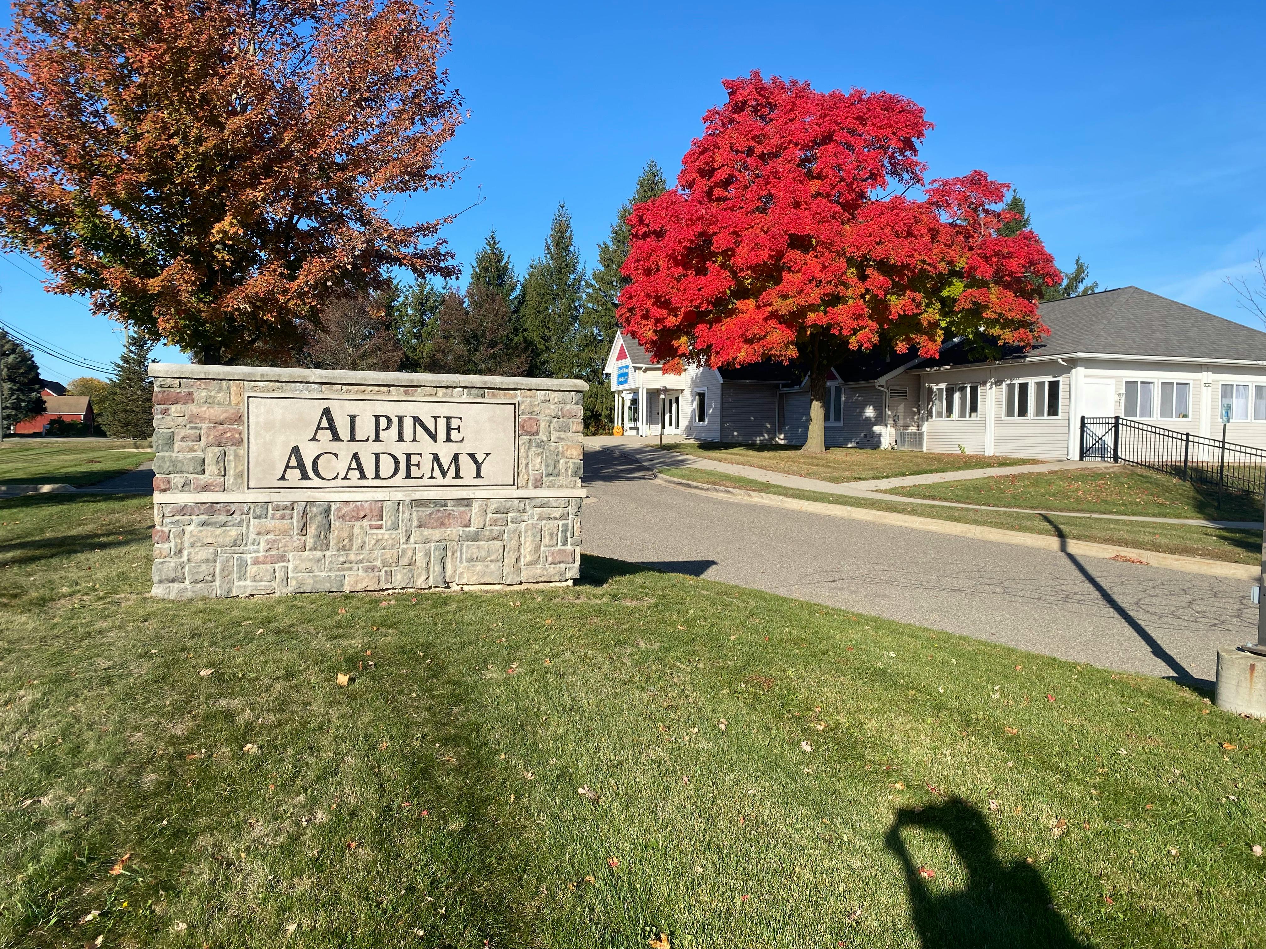 Alpine Academy sign in front of a building with a red tree