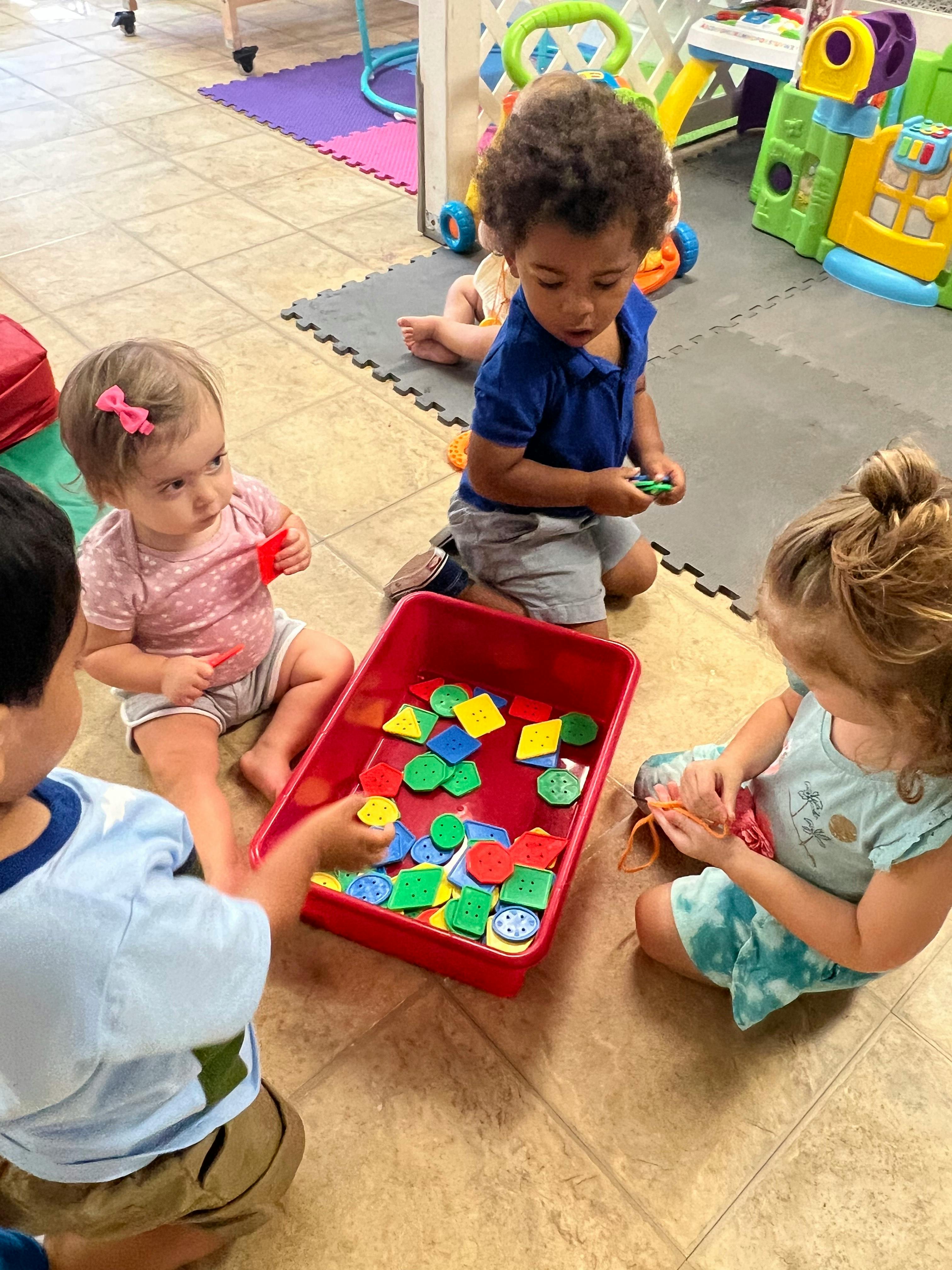 Four children playing with colorful shape cutouts from a red tray