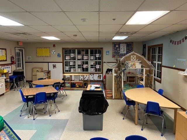 empty classroom with small tables and chairs, a play barn in the corner