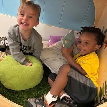 Two children sitting together in a cozy nook with a book