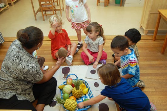 Adult and children sitting on floor with basket of fruit