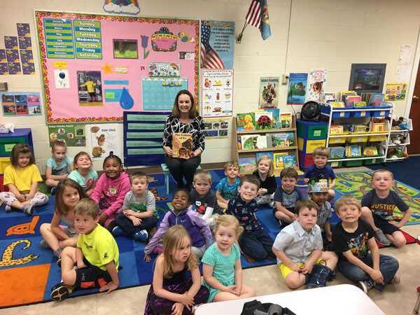 Adult holding a book surrounded by children in a classroom