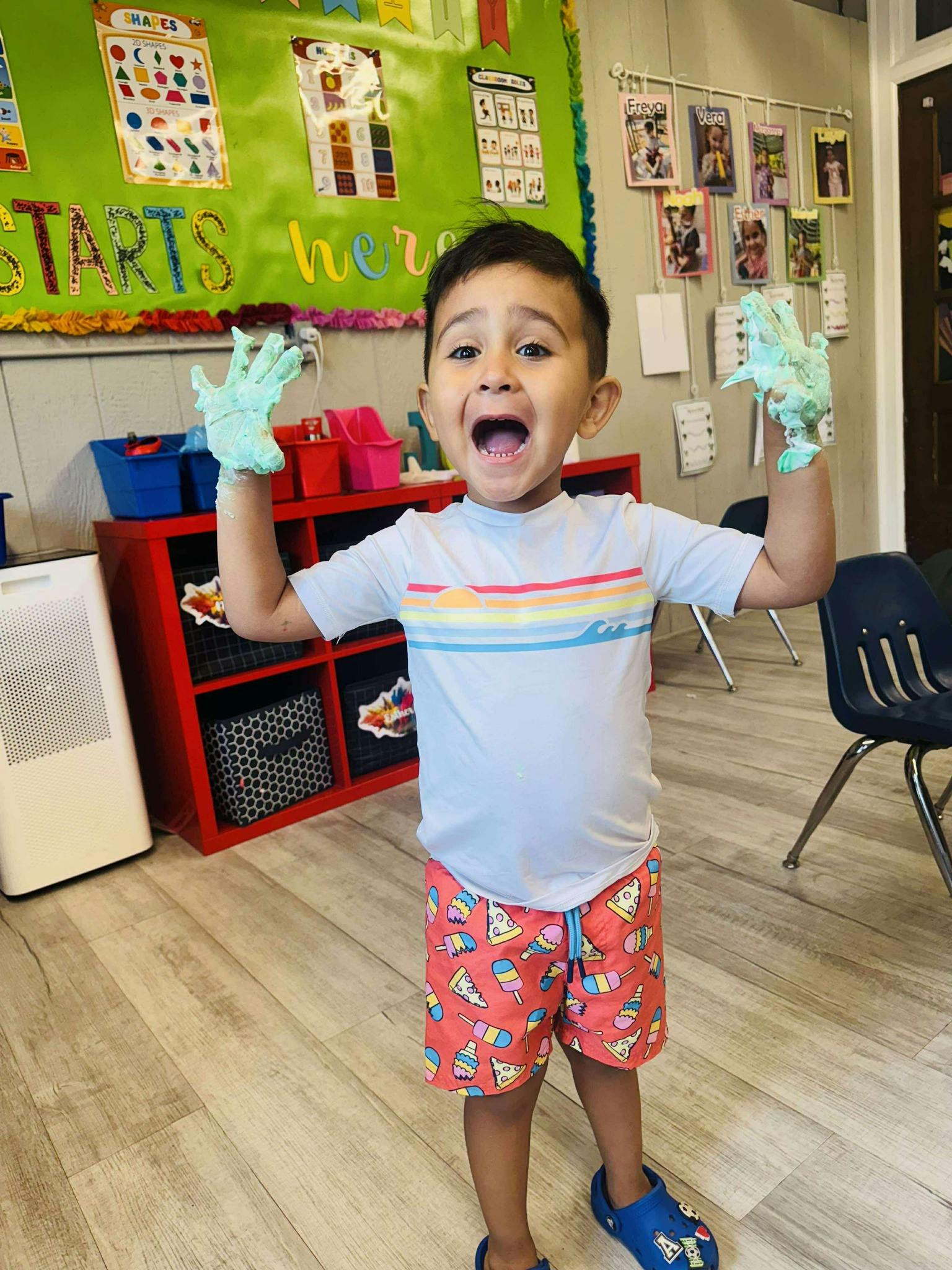 Child with hands covered in light blue paint, mouth open