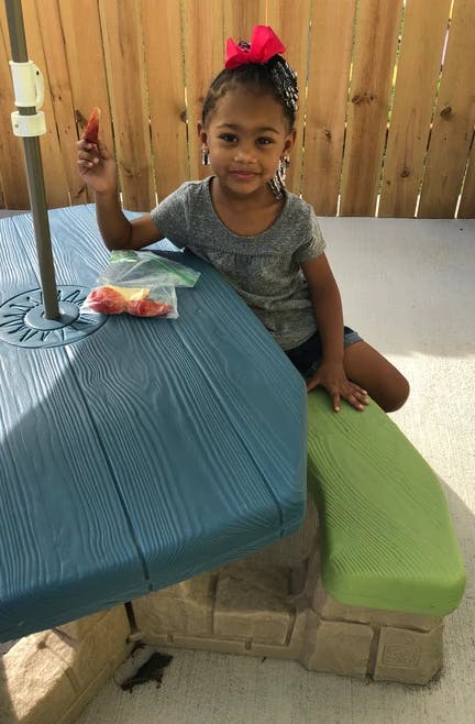 Child sitting at a picnic table holding a piece of fruit