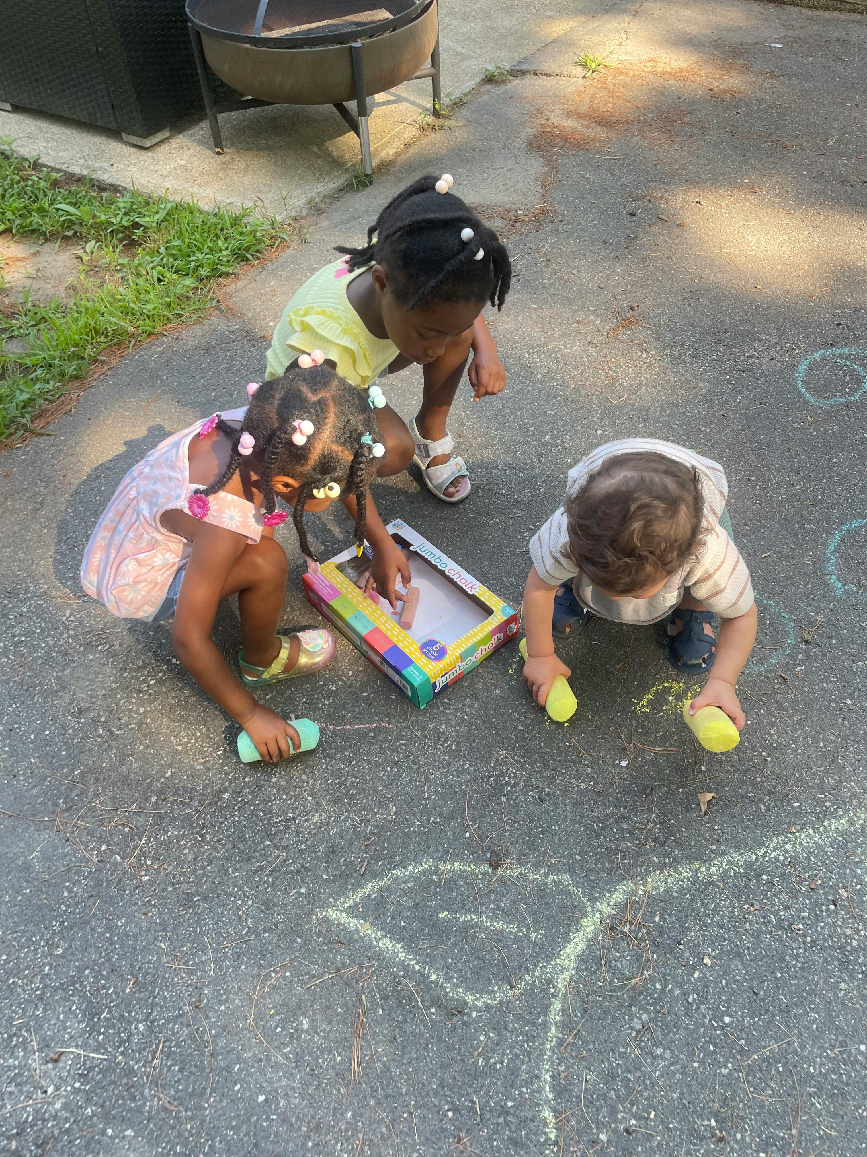 Three children drawing with chalk on pavement