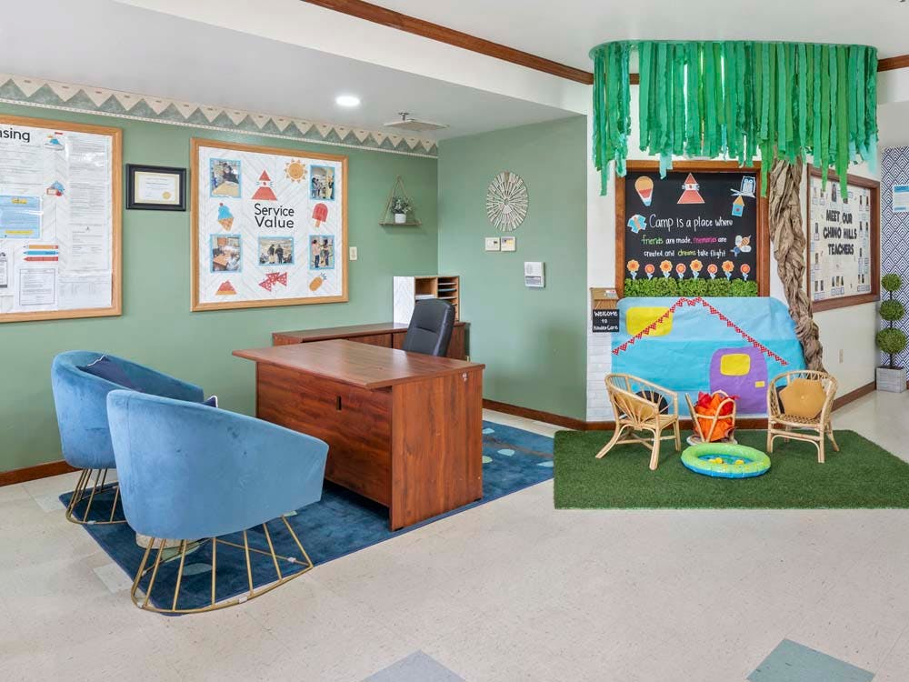 Office with a desk, two blue chairs, bulletin boards, and a play area