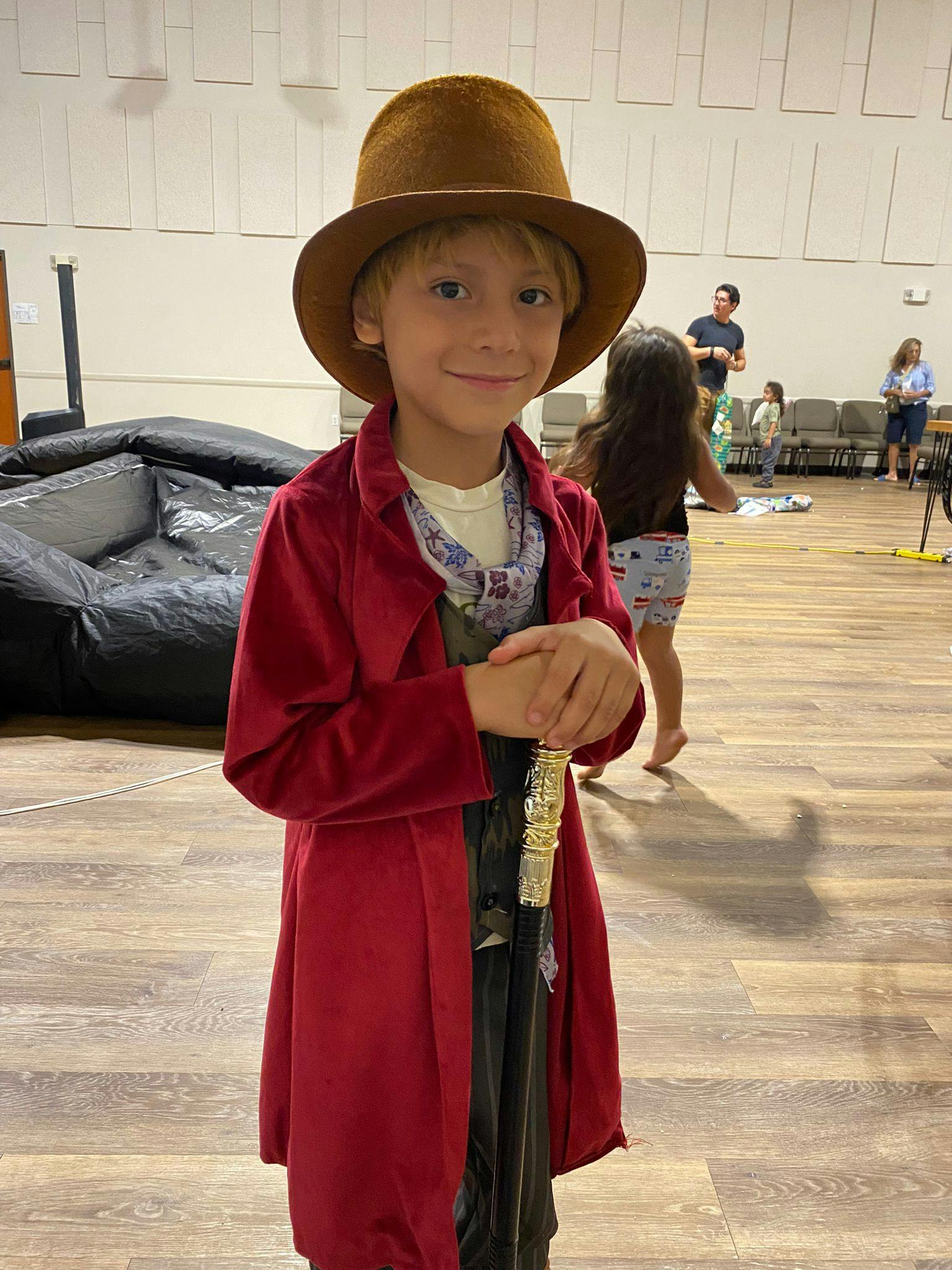 Child in a brown hat and red coat holding a cane