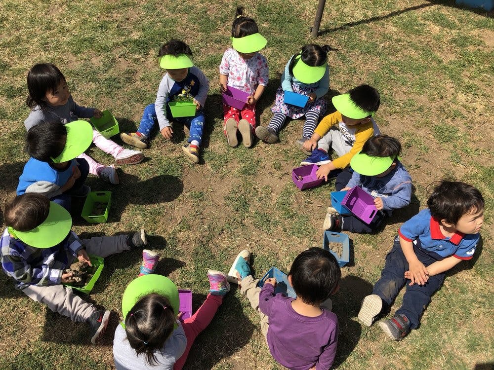 Children sitting in a circle on grass, some wearing green visors