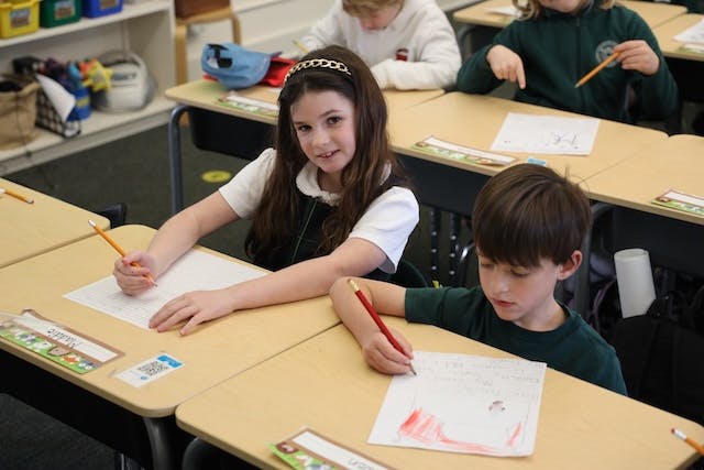 Children writing and drawing at desks in a classroom