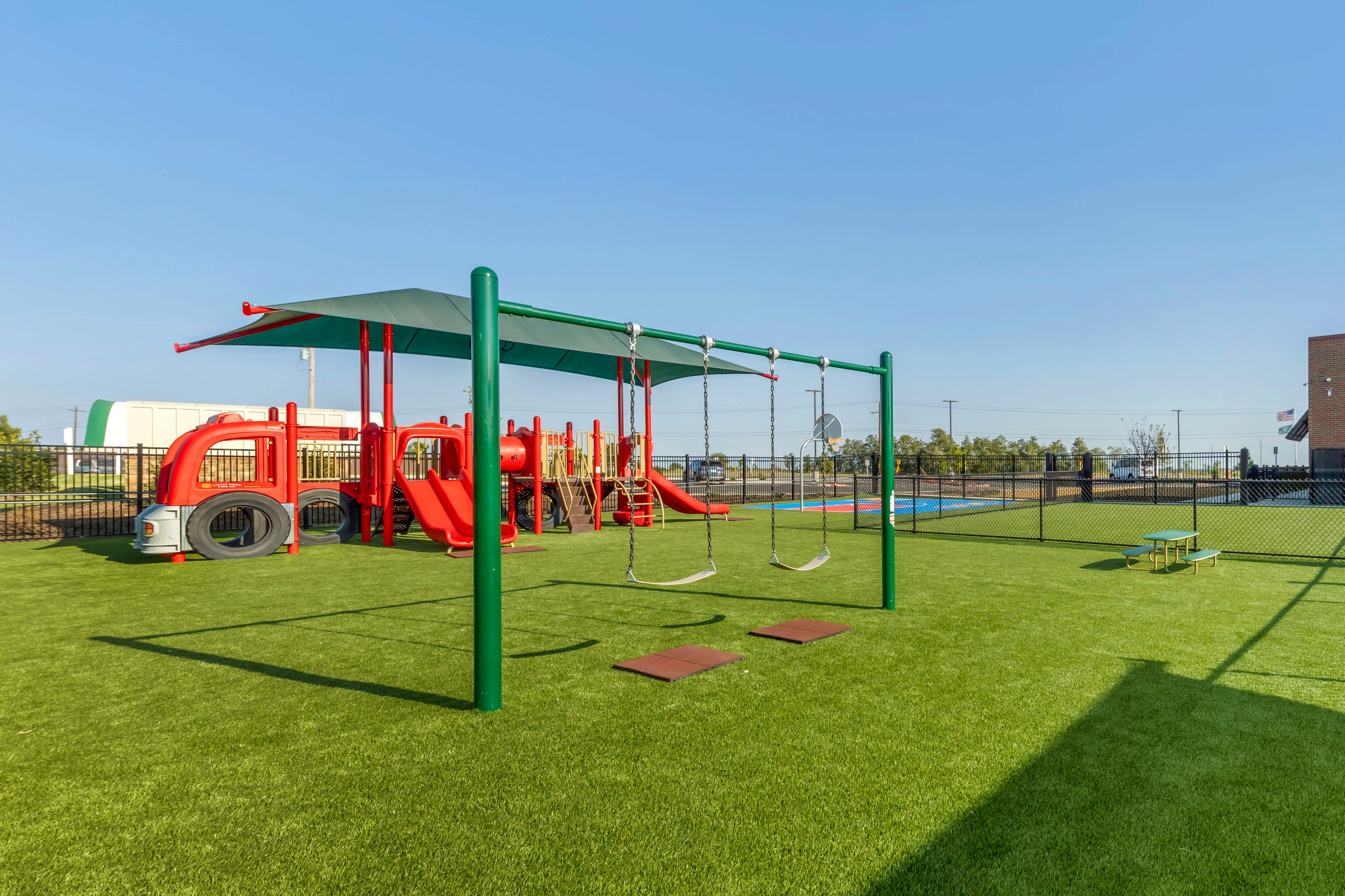 Playground with red slides, green shade structure, swings, and artificial turf