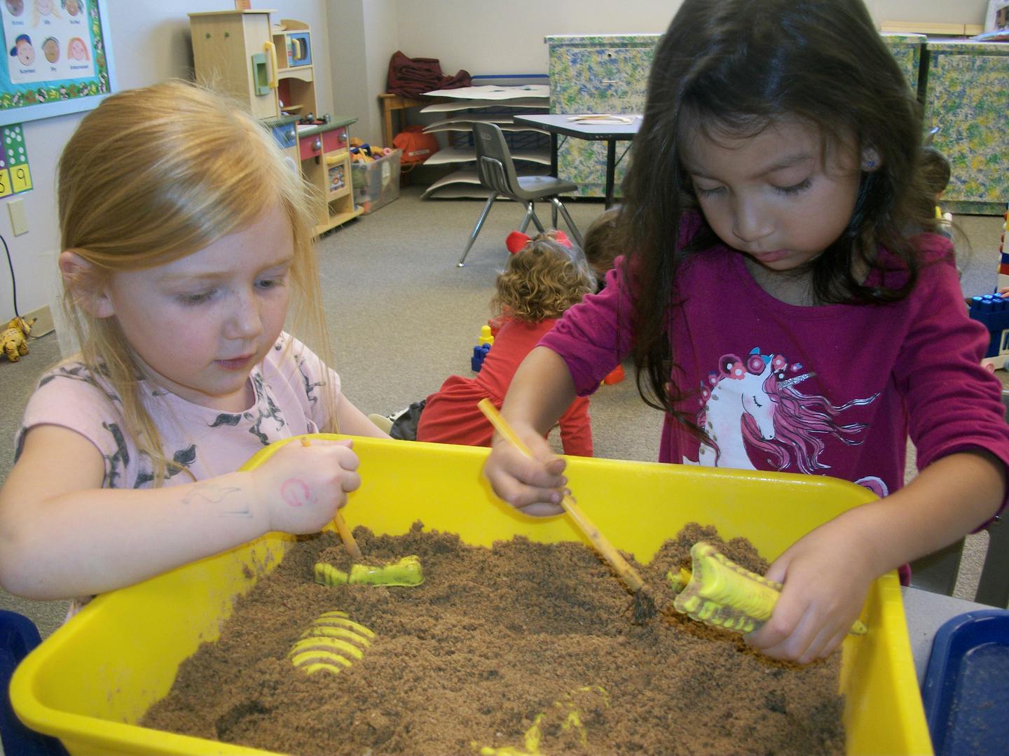 Two children playing in a sand table with toys