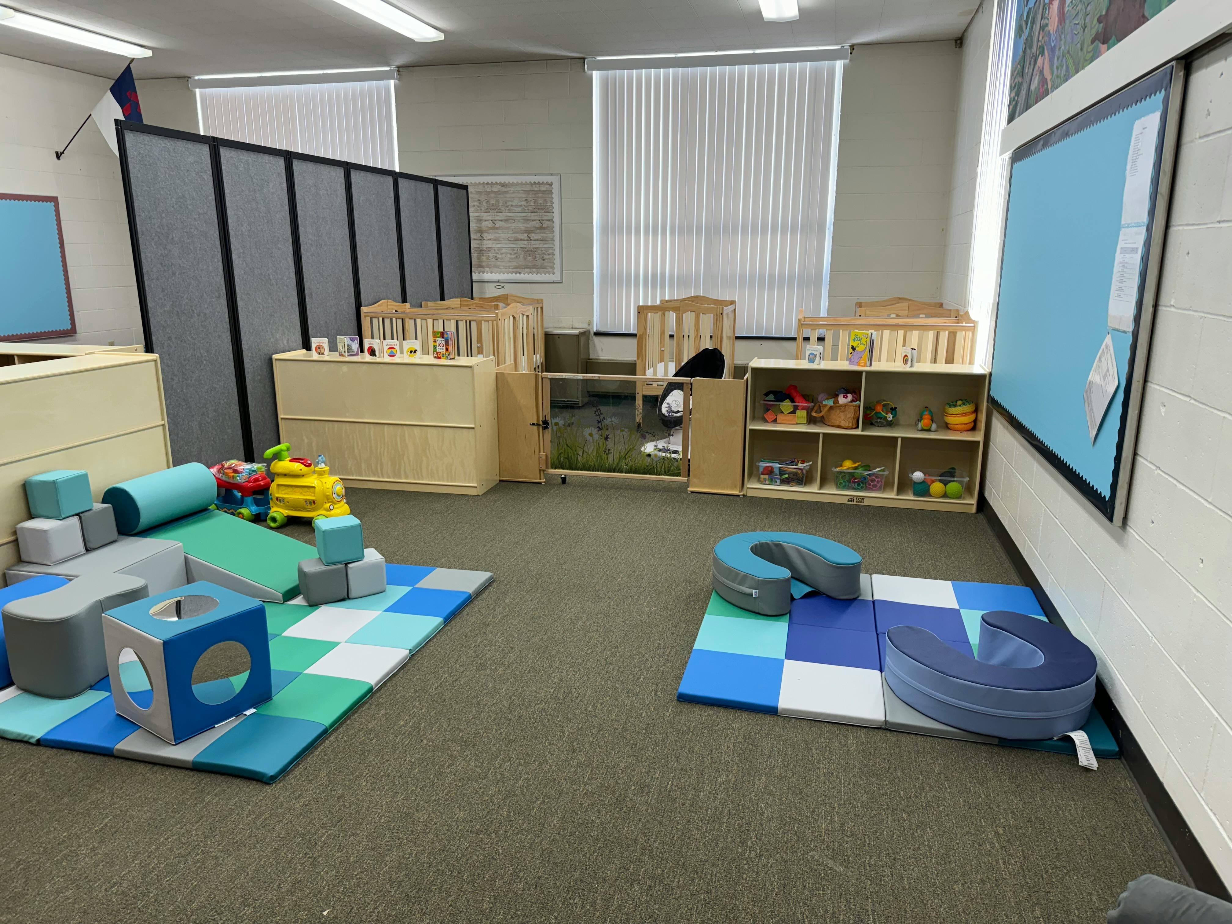 Playroom with soft play equipment on checkered mats and cribs in the background