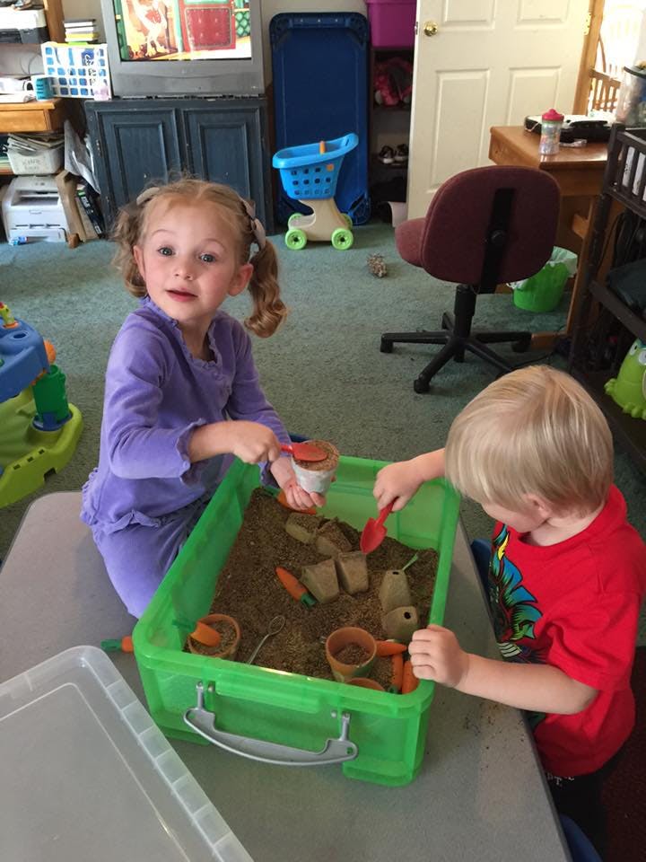 Two children playing with a sensory bin filled with dirt and small pots