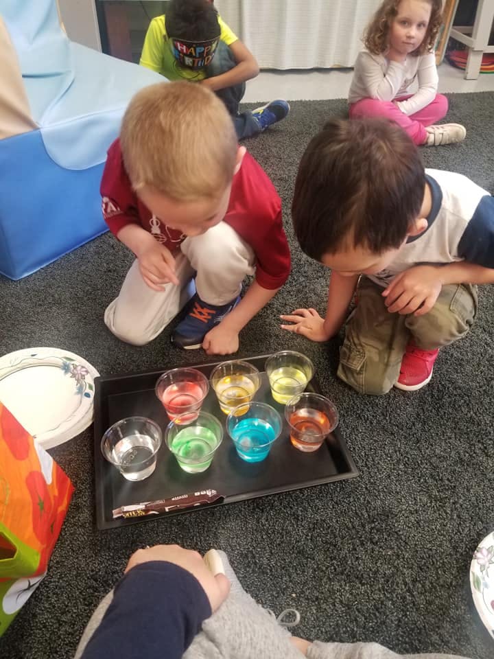 Children looking at cups with colorful liquids on a tray