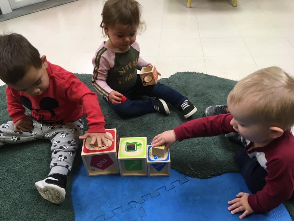Three children playing with stacking blocks on a rug