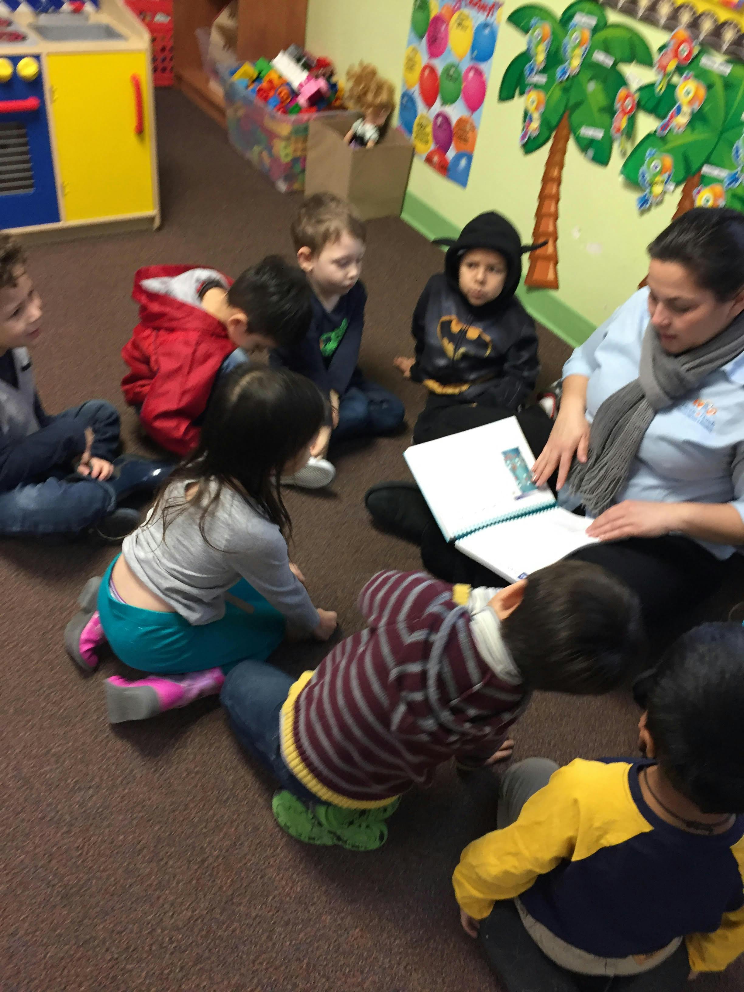 Adult reading a book to a group of children sitting on the floor