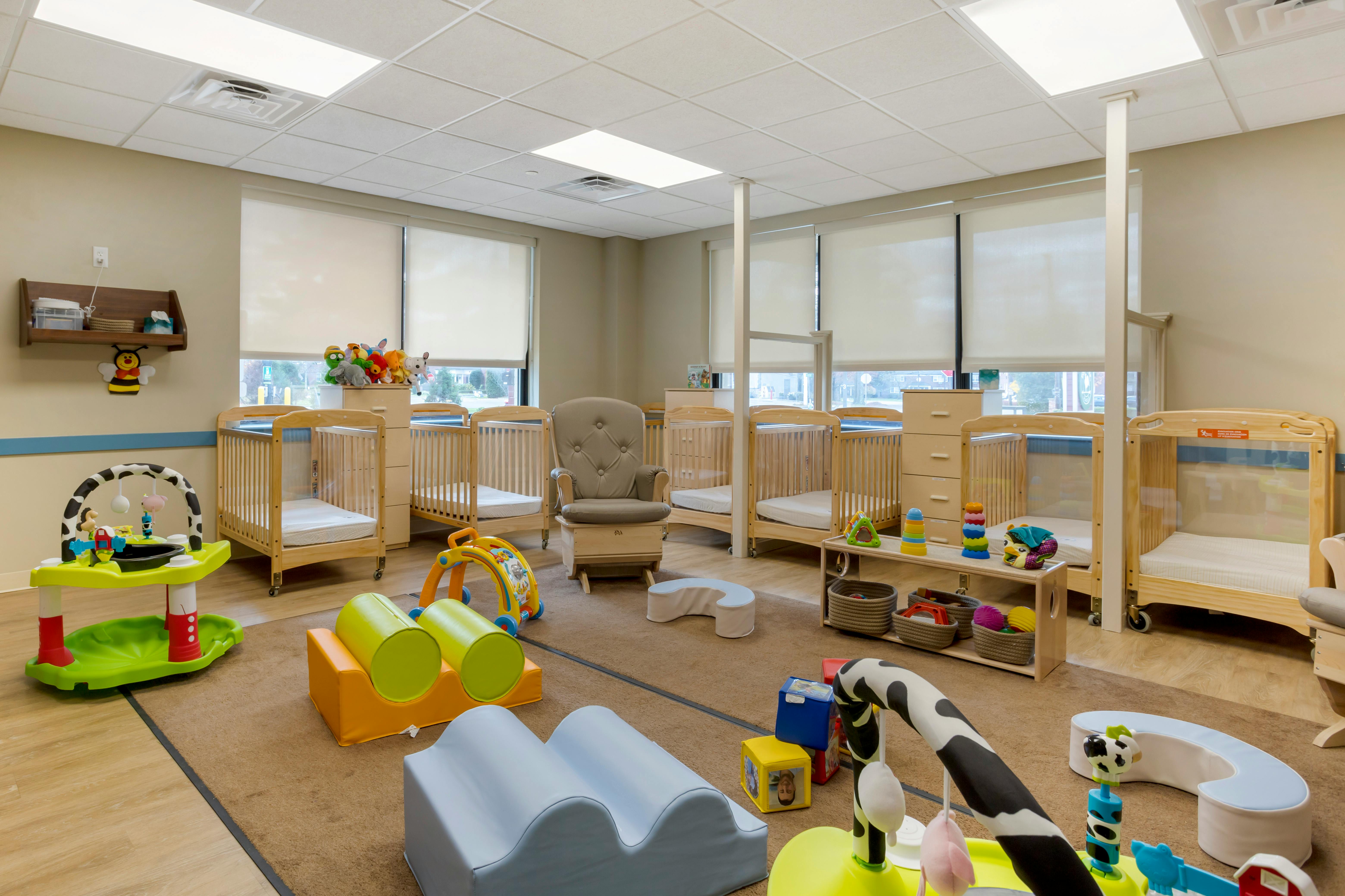 A room with several cribs, a glider chair, and various baby toys on the floor