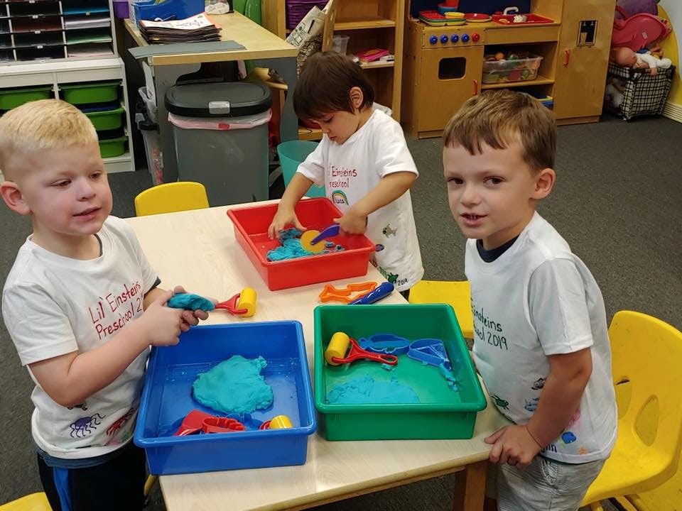 Three children playing with colorful toys and sensory bins at a table