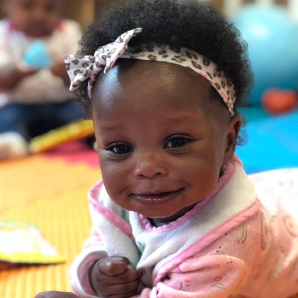 Child wearing a leopard print headband and pink outfit, white, and blue clothing