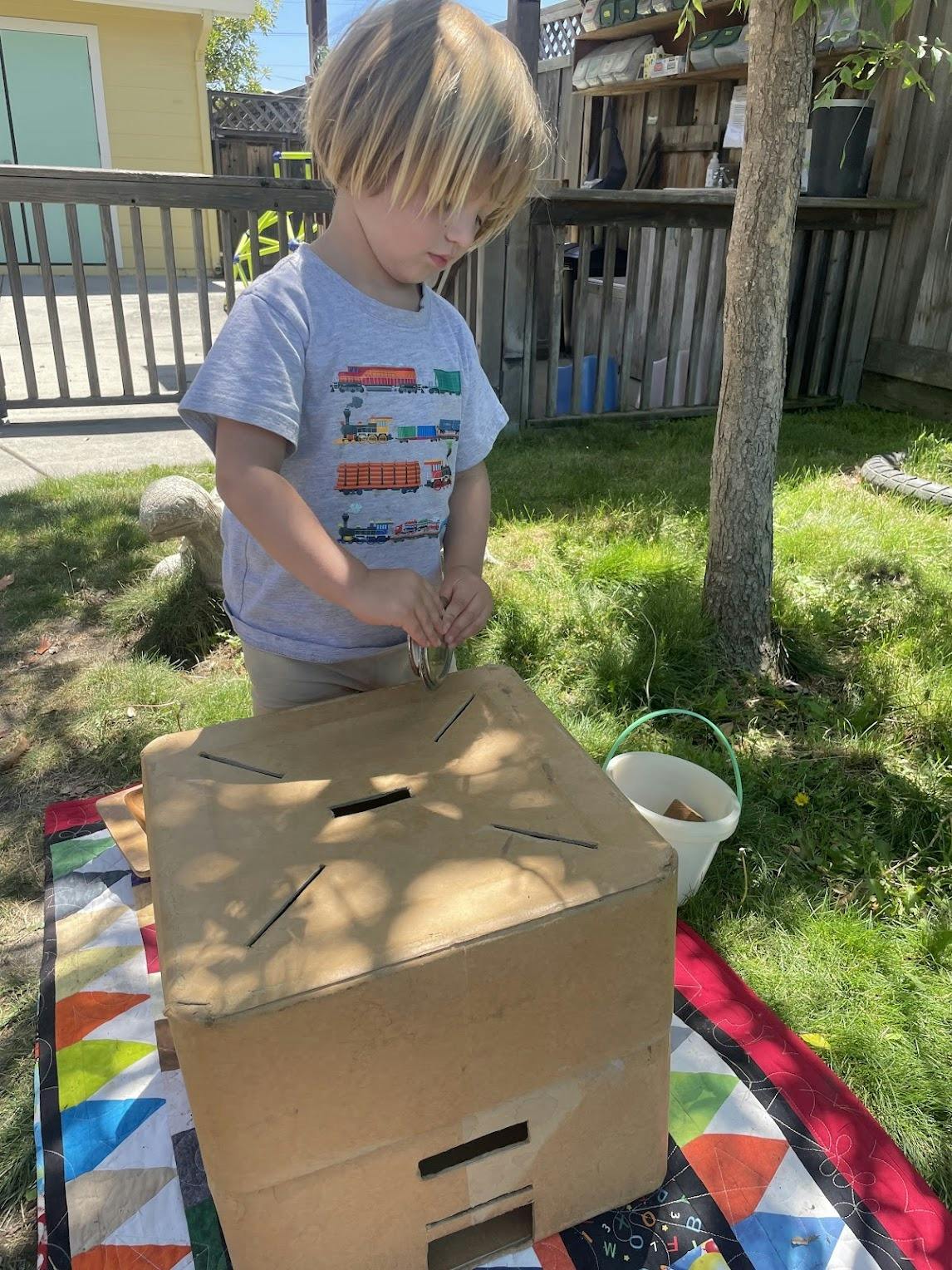 Child putting an object into a cardboard box in a yard