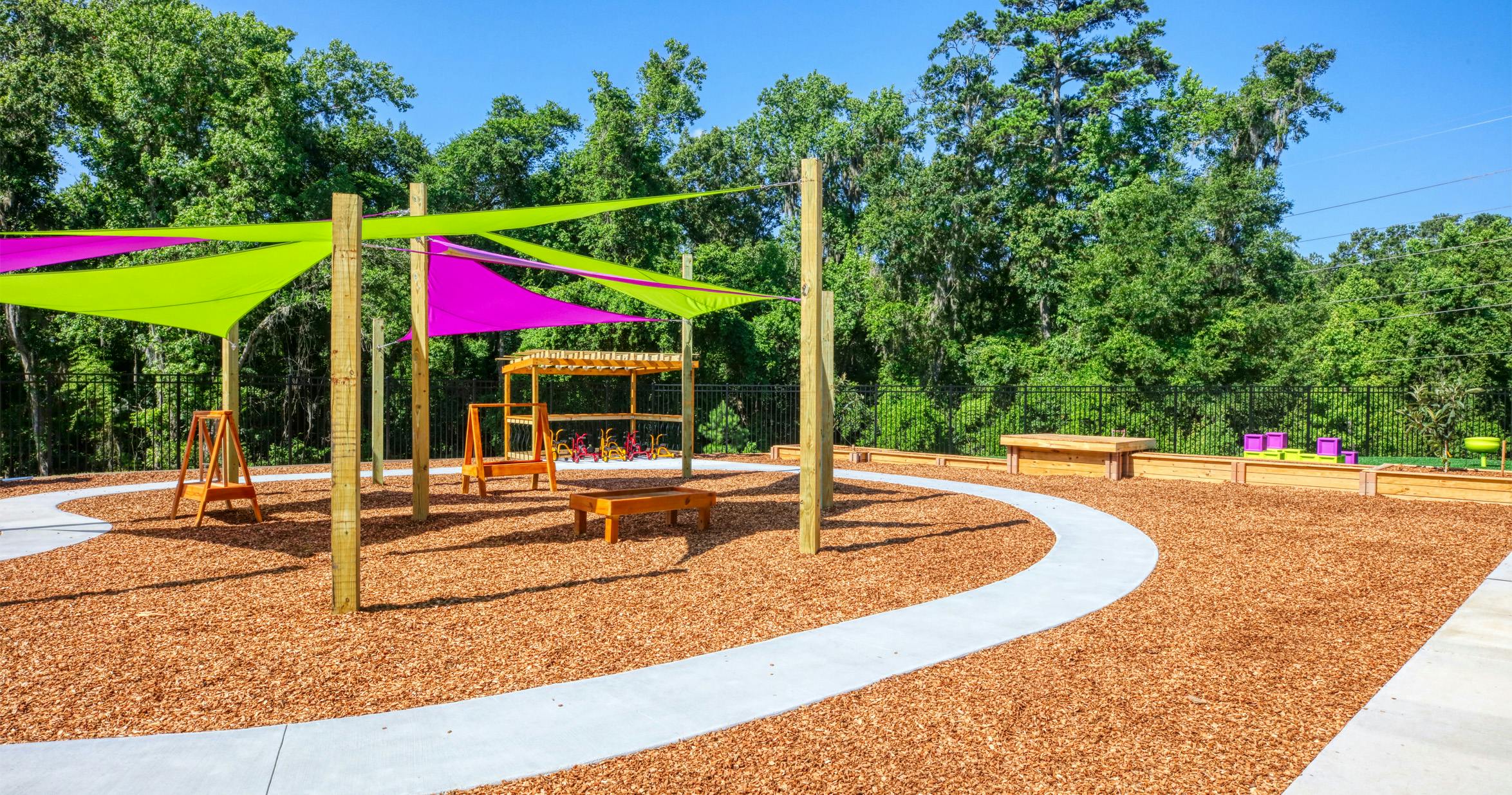 Outdoor playground with colorful shade sails, wood chip ground, and small tricycles