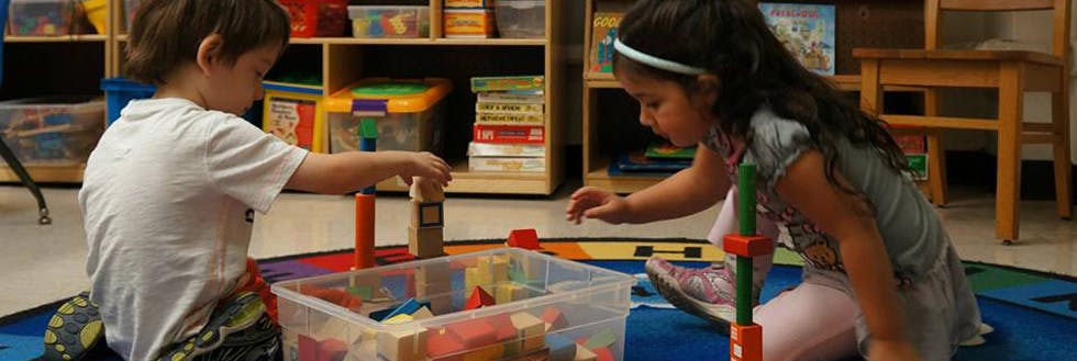 Two children playing with blocks on the floor in a classroom
