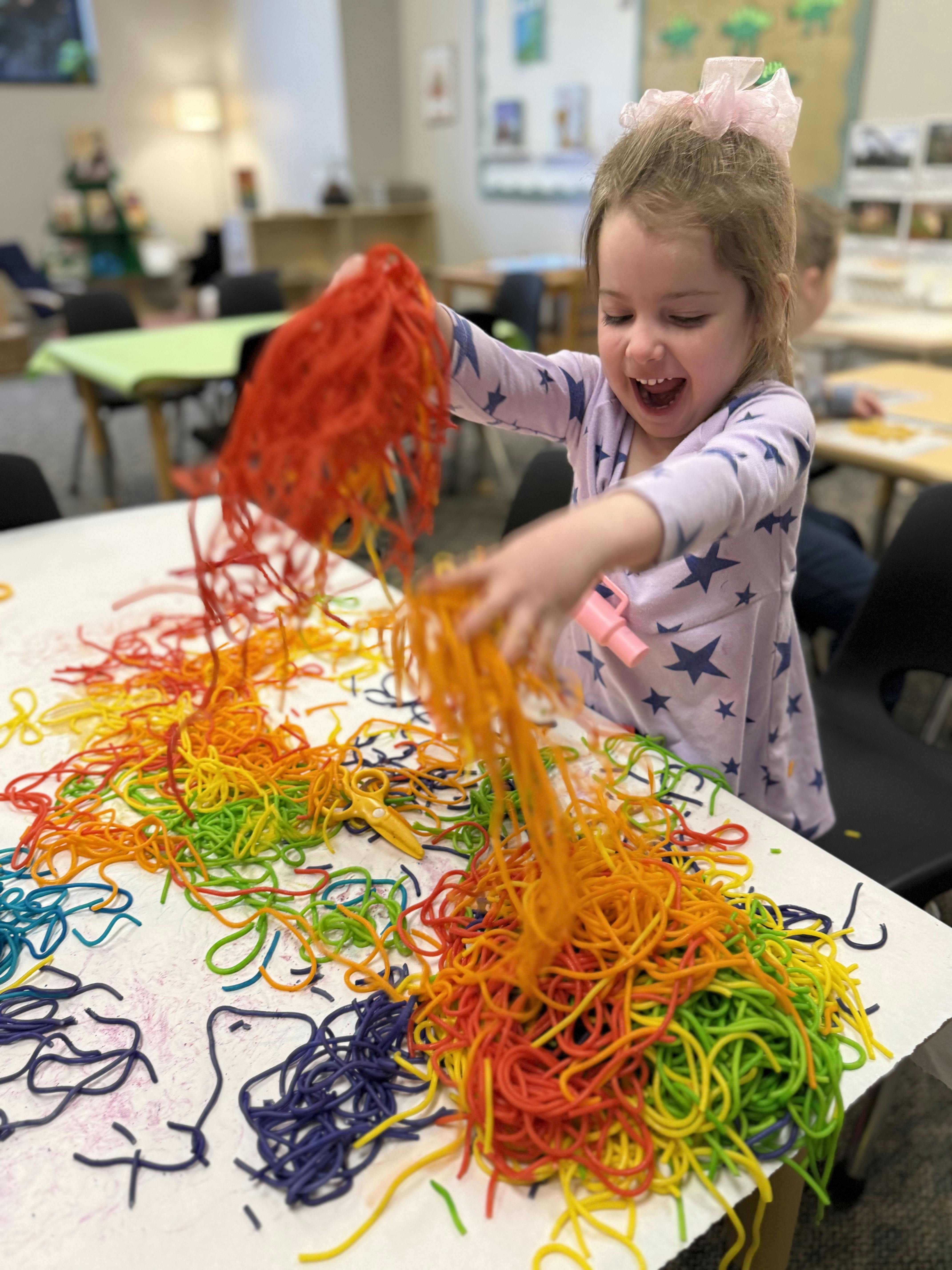 Child playing with colorful strands of pasta on a table