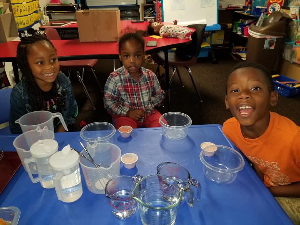 Three children at a table with measuring cups and containers
