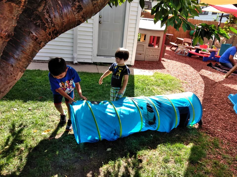 Two children playing with a blue tunnel on grass