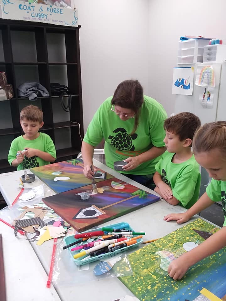 Adult and children painting on canvases at a table