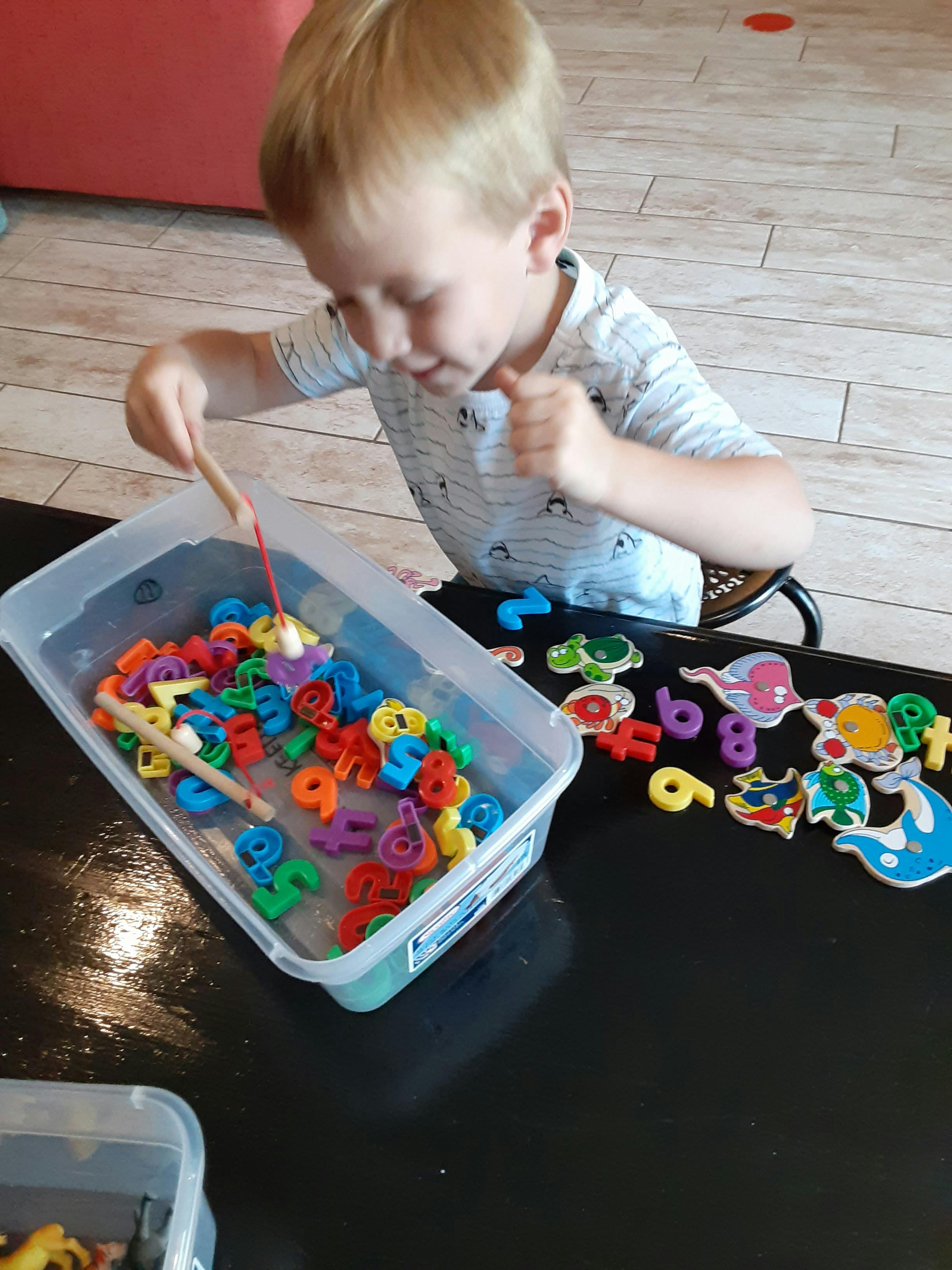 Child playing with colorful magnetic letters and numbers in a container