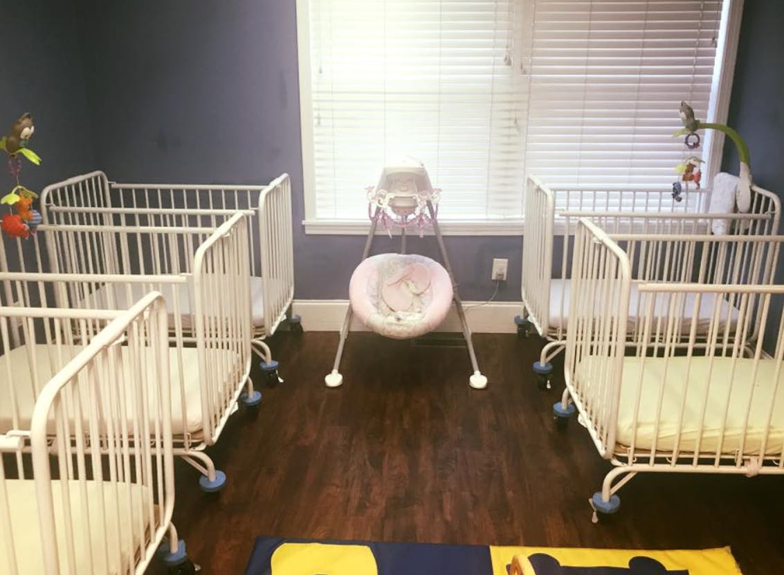 Two cribs and a baby swing in a room with a window
