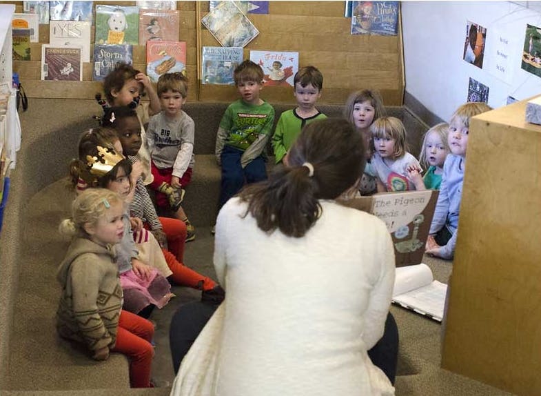 Person reading a book to a group of children in a classroom