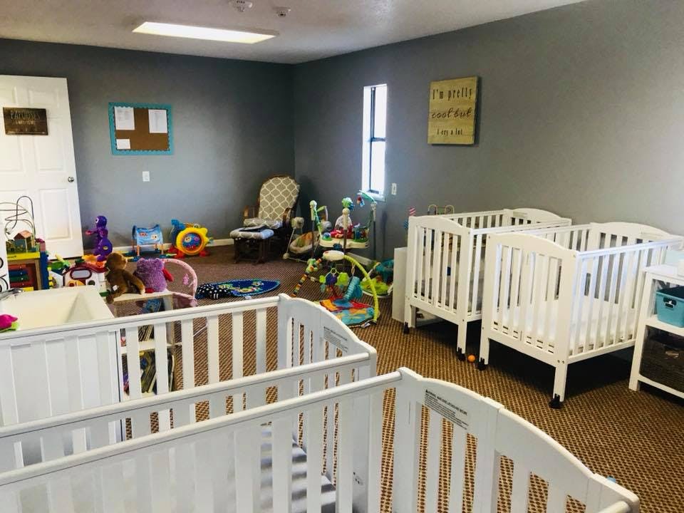 Multiple white cribs in a room with toys on the floor