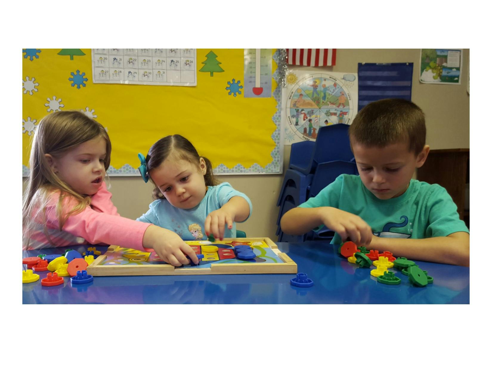 Three children playing with colorful blocks at a table in a classroom