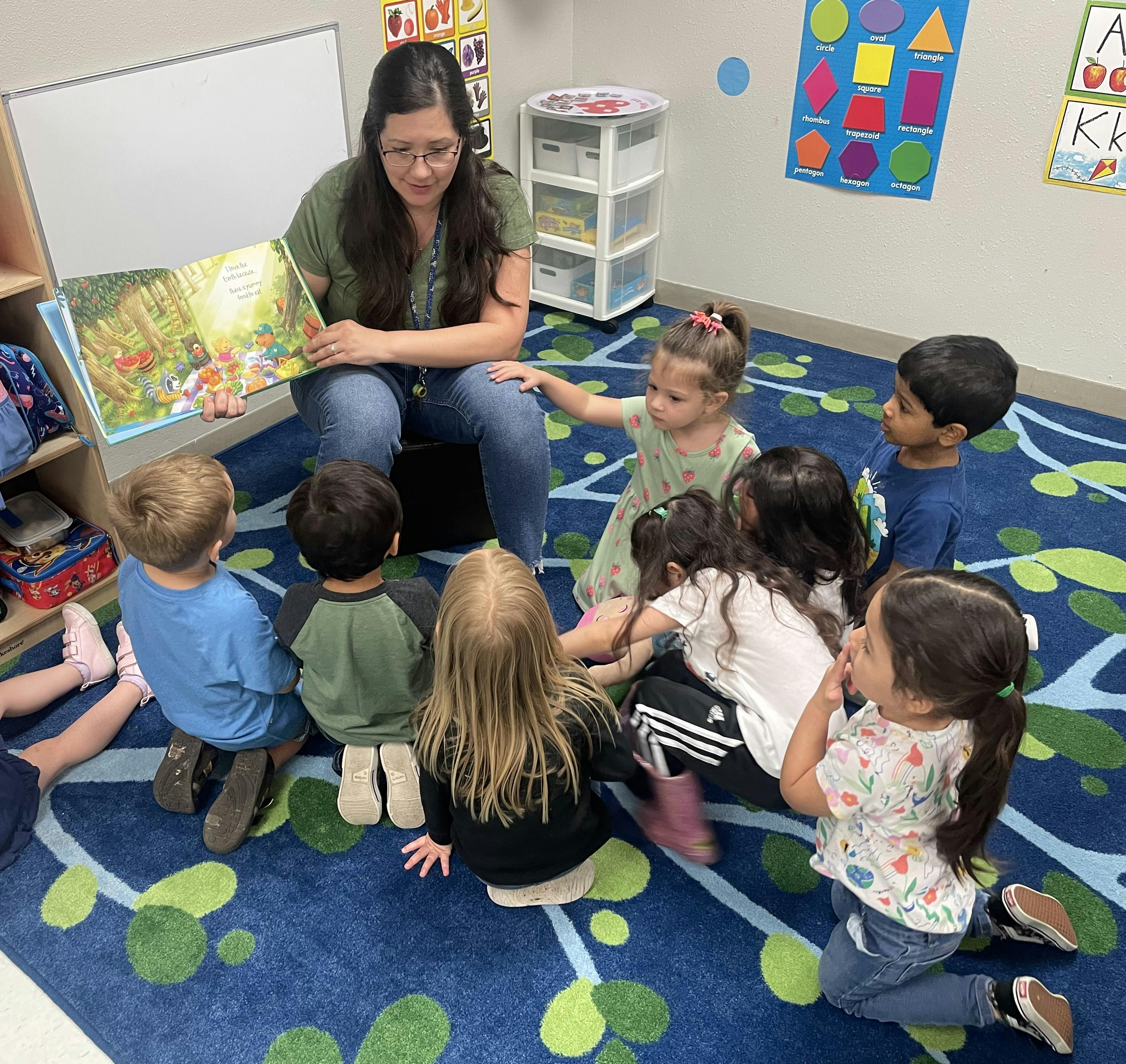 Person reading a book to a group of children sitting on a rug