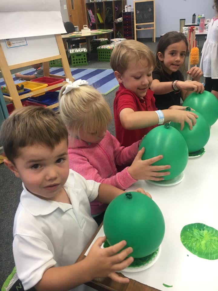 Children holding green balloons in a classroom