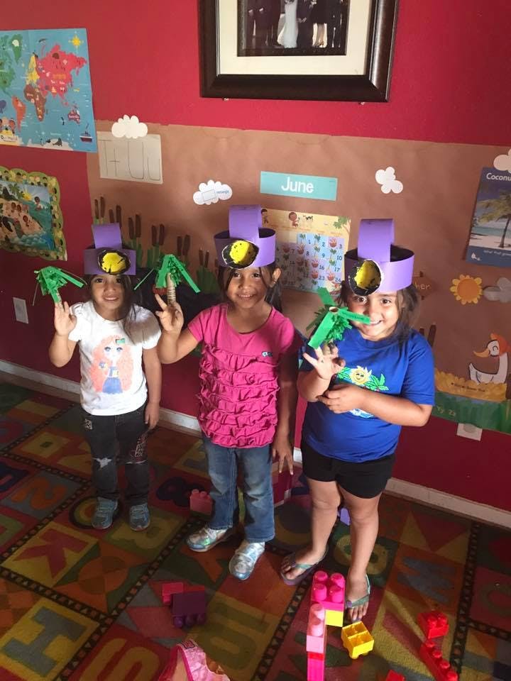 Three children wearing paper hats and holding green paper crafts