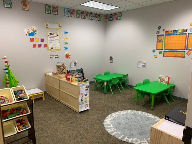 Classroom with small green tables and chairs, storage units, and wall decorations