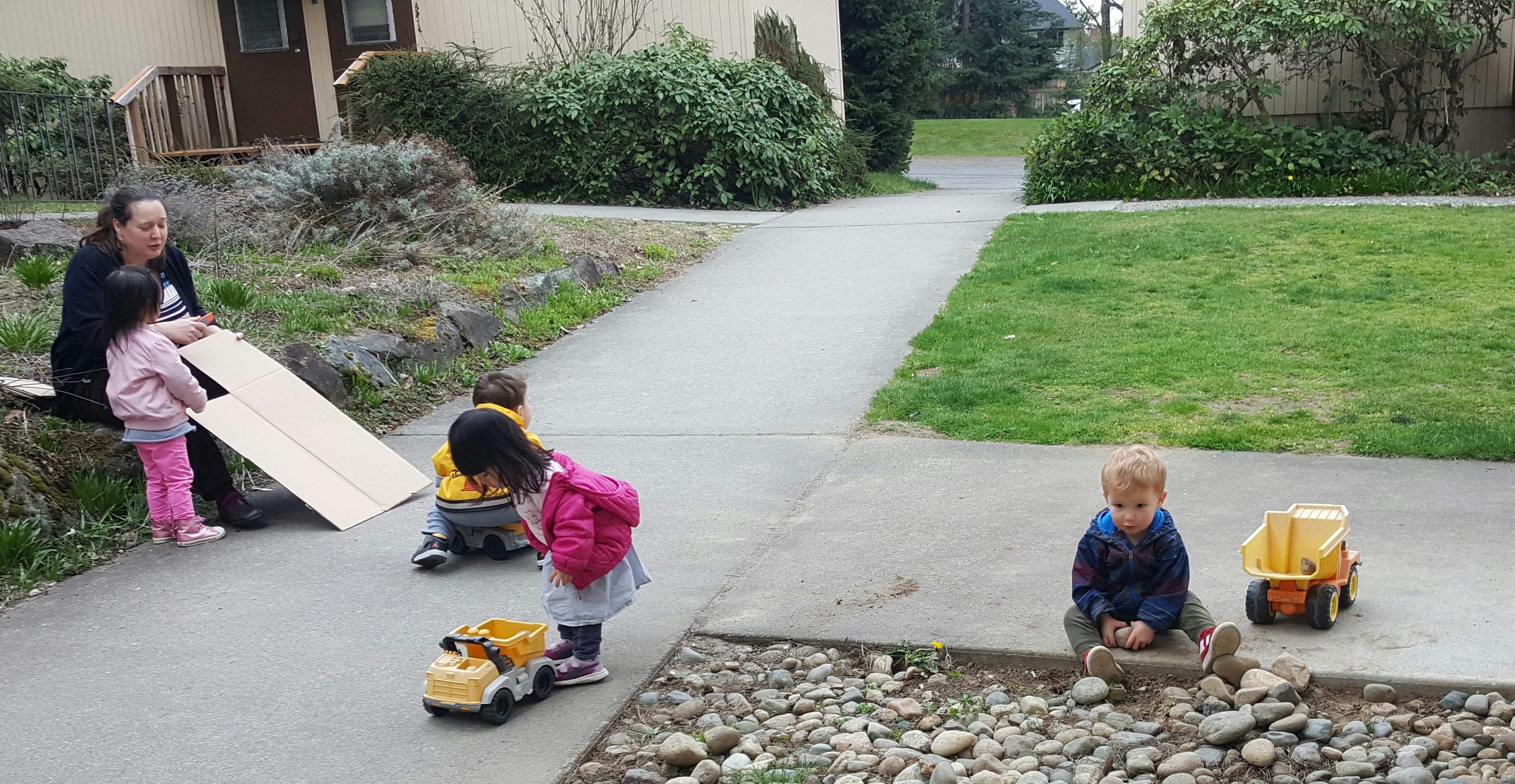 Adult and children playing with a wooden board and toy trucks outdoors