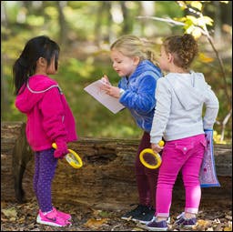 Three children looking at a paper outdoors