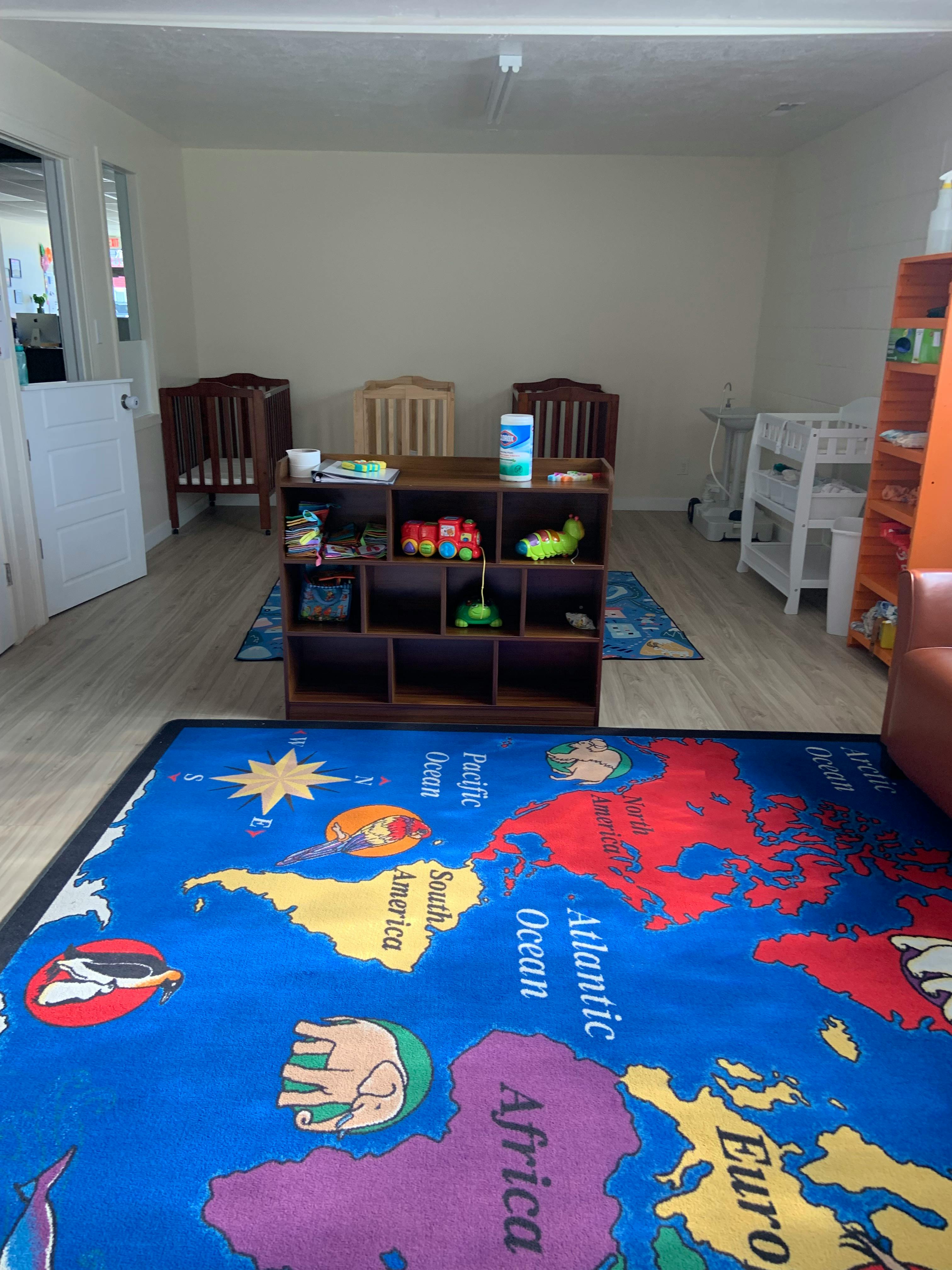 Playroom with a world map rug, cribs, and toy shelves