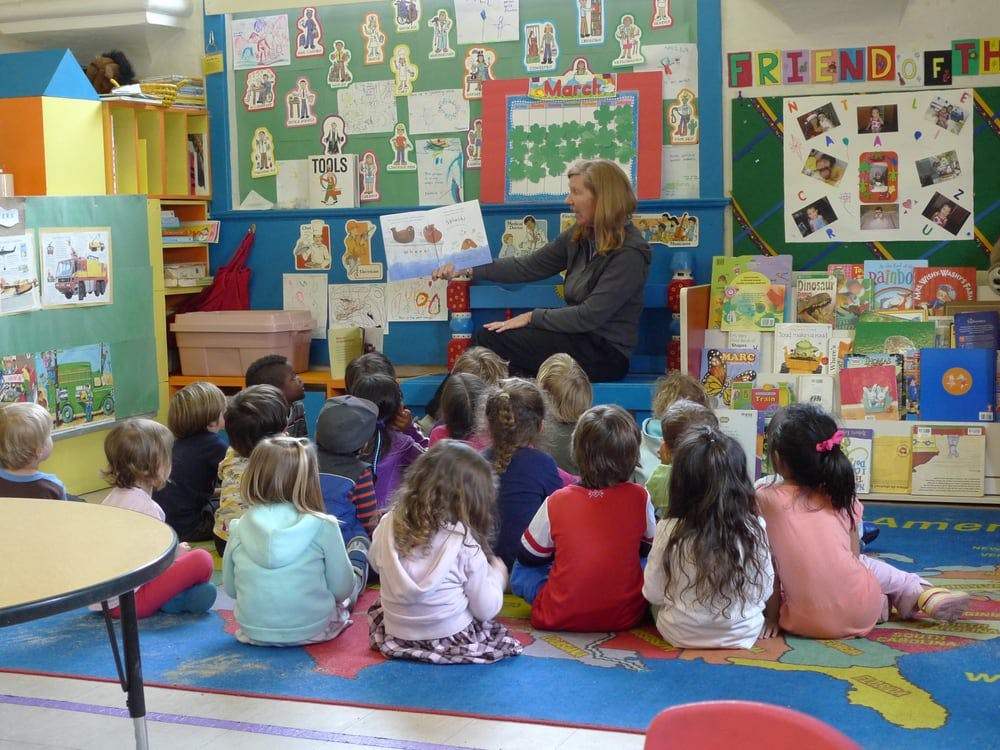 Person reading a book to a group of children in a classroom