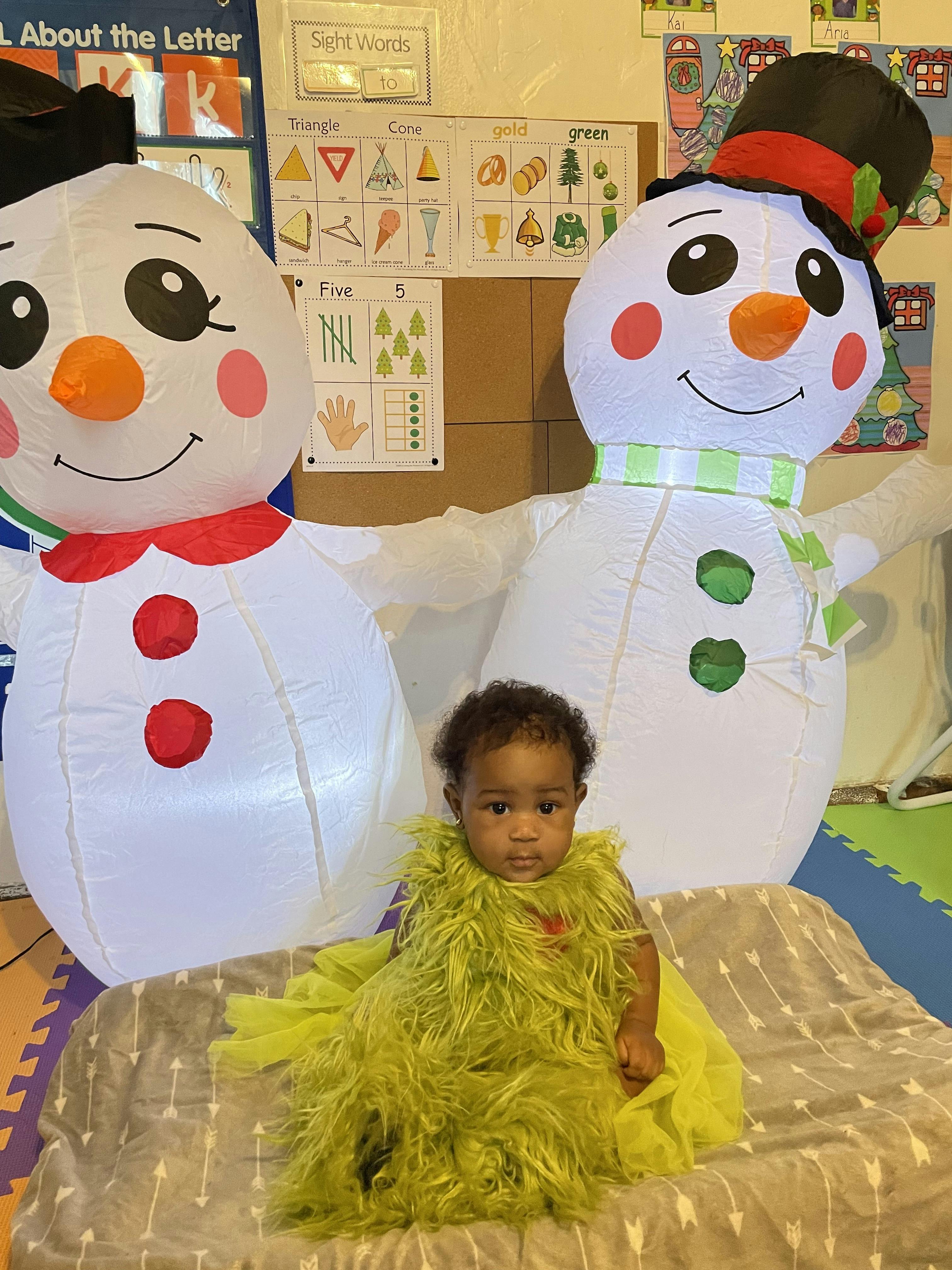 Child in a green costume sitting between two inflatable snowmen