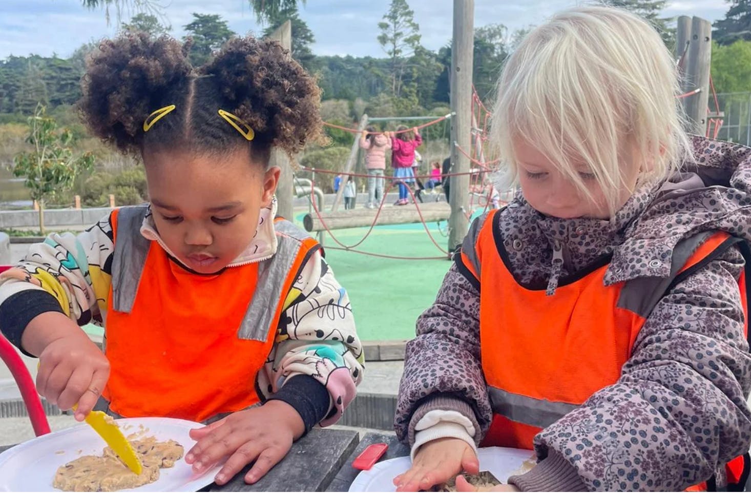 Two children in orange vests playing with food on plates