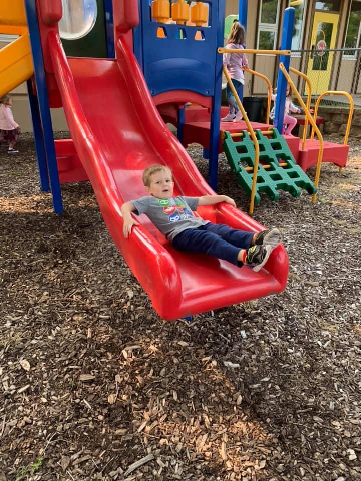 Child sitting at the bottom of a red playground slide