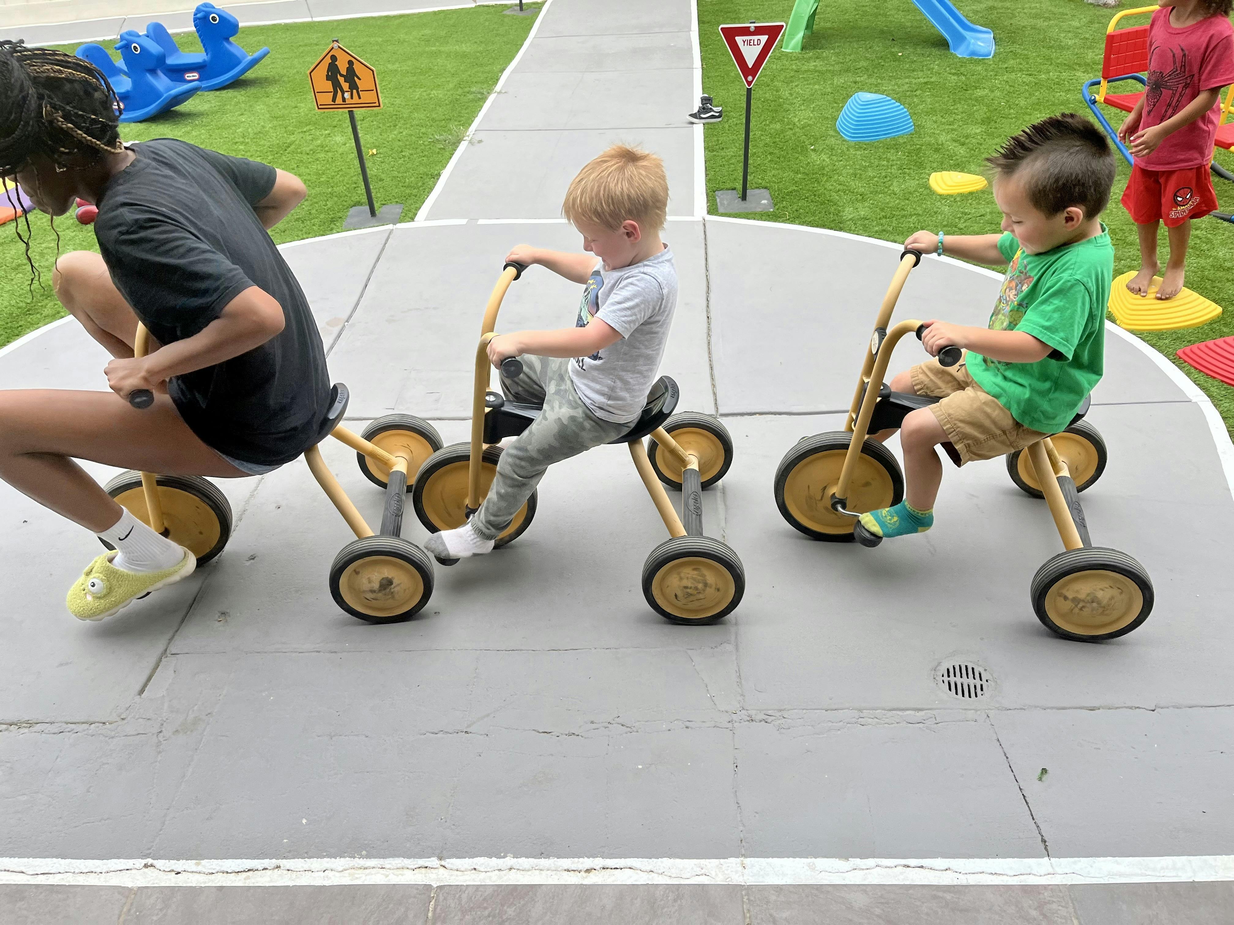 Person and two children riding tricycles on a paved path